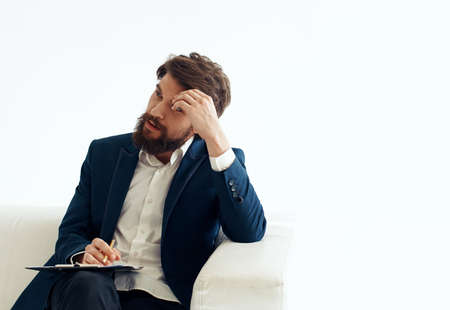 A business man in a suit with documents in his hands on a connected uniform sits on a sofa indoors