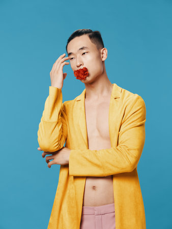 Man with a red flower in his mouth yellow jacket nude torso blue backgroundの写真素材