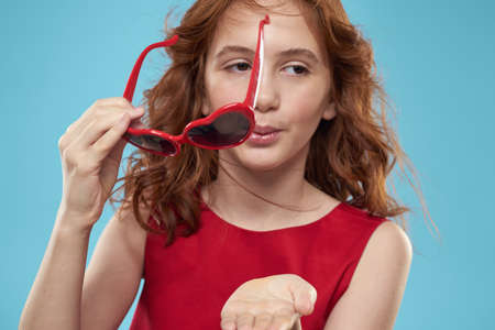 Little girl in sunglasses in the form of hearts red dress curly hair blue background