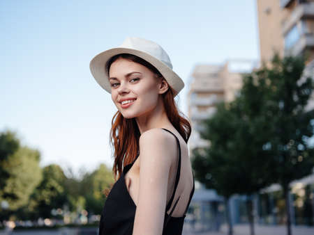Pretty woman in a black T-shirt and hat are walking on the street near the buildingの写真素材