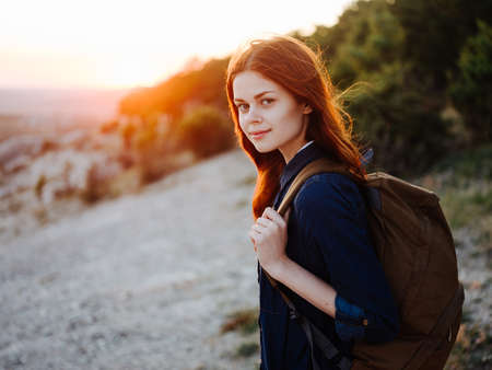 Hiker in the mountains with a backpack on her back sunset and trees nature
