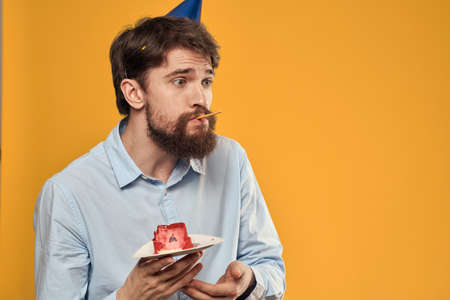 Man with cake on yellow background birthday party hat cropped viewの写真素材