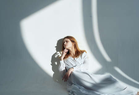 A woman in a dress In a bright room, red hair, a falling shadow