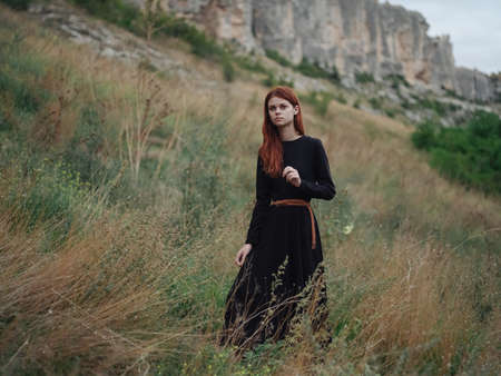 Traveler in the woods on a meadow in the mountains black dress red hairの写真素材