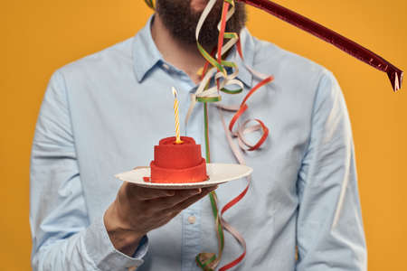 Guy with a cake in a plate on a yellow background holidays candle cropped viewの写真素材