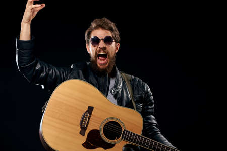 man with a guitar in his hands black leather jacket sunglasses music emotions black backgroundの写真素材