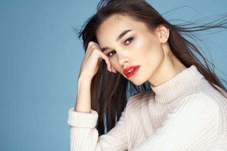 Brunette in a white sweater red lips charm long hair blue background