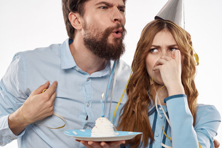 energetic man and woman with a cake and in hats celebrate a birthday on a light backgroundの写真素材