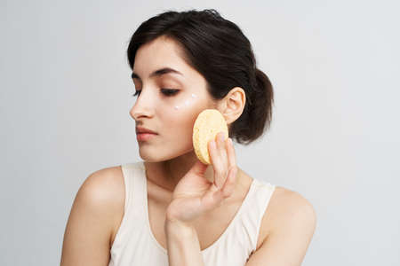 pretty brunette cleanse skin with sponge rejuvenation care light backgroundの写真素材