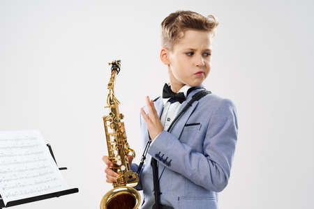 boy musician in a classic suit holds a saxophone in his hand on a white backgroundの写真素材