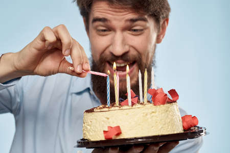 Man with a plate of cake and a festive candle blue background cap corporate partyの写真素材