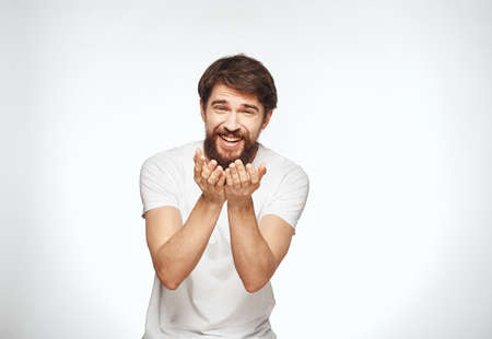 Happy man gestures with his hands on a white background in a light T-shirtの写真素材