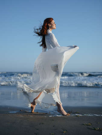 Portrait of a woman in a dress by the ocean on the beach, in full growthの写真素材