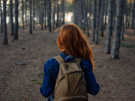 Back view of a woman with a backpack and in a blue shirt on nature in the forest