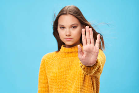 woman on a yellow sweater holds her hand in front of her emotions blue backgroundの写真素材