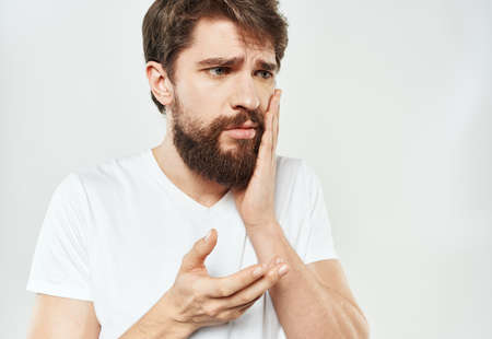 An emotional man in a white T-shirt gestures with his hands on a light backgroundの写真素材