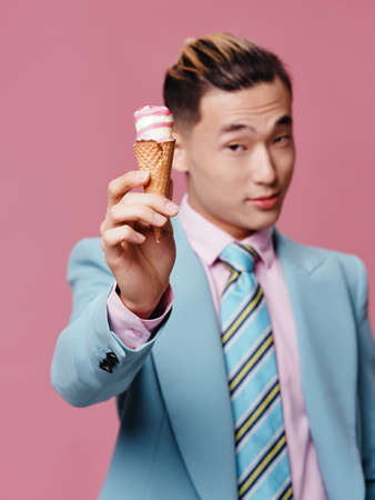 man asian appearance ice cream in hands blue suit pink background enjoymentの写真素材