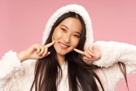 happy asian woman touching face with fingers and white sweater pink backgroundの写真素材