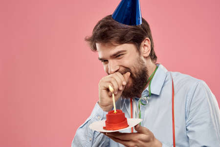 Man with a cake with a candle and a birthday cap on a pink backgroundの写真素材
