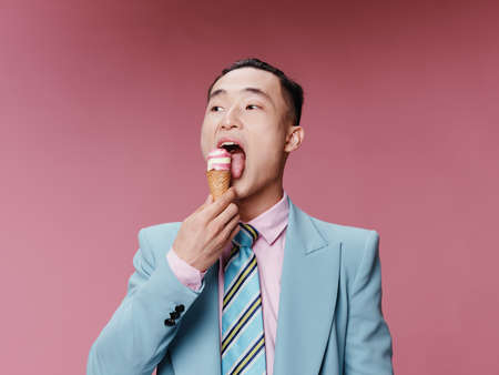 A man in a classic suit tastes ice cream on a pink backgroundの写真素材