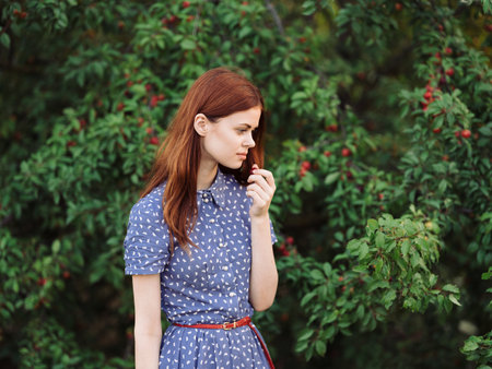 Portrait of a romantic woman in a blue dress near green bushes with red berriesの写真素材