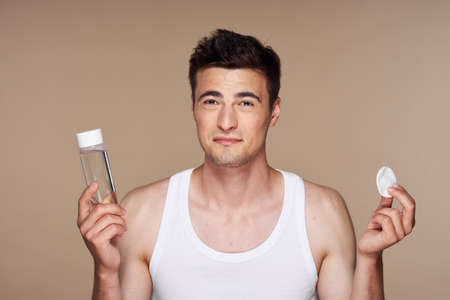 man with lotion and cotton in hand on beige background clean skin cosmetologyの写真素材