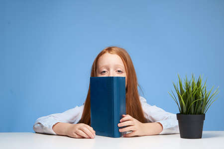 red-haired girl sitting at the school table book in hands education