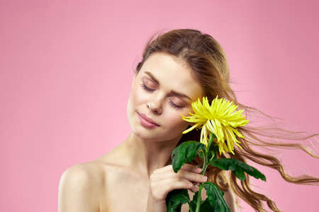 Beautiful girl with a yellow flower on a pink background nude shoulders makeupの写真素材