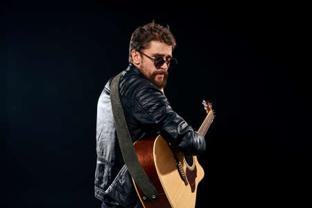 man with a guitar in his hands black leather jacket sunglasses music emotions black backgroundの写真素材