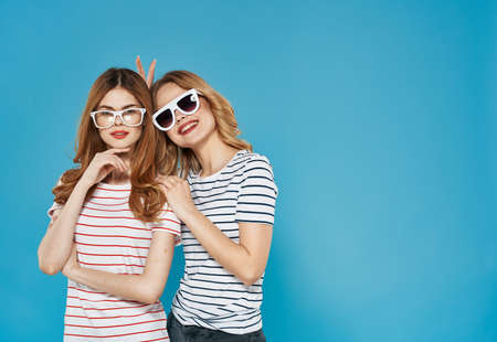 two sisters stand side by side fashionable clothing studio luxury friendship blue backgroundの写真素材