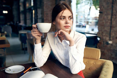 beautiful woman with a cup in hand sits at a table in a cafe and book a restaurantの写真素材