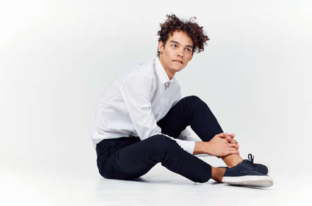 a teenager in a suit and sneakers sits on the floor In a bright room side viewの写真素材