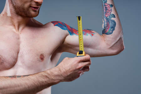 guy measures arm muscles with centimeters on a gray background and a multicolored tattoo bodybuilder fitnessの写真素材