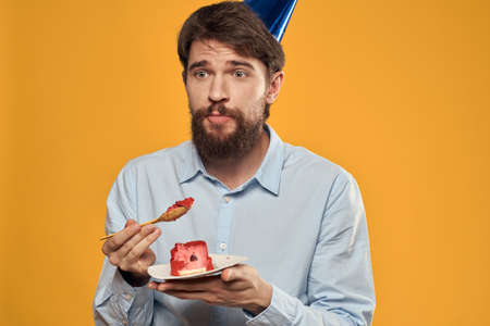 a man with a birthday cake in his hands and in a cap on a yellow background on his birthdayの写真素材