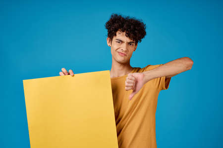 guy with curly hair holding a yellow poster in his hands advertising