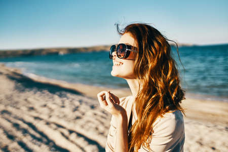 side view of red-haired woman model in shirt and glasses near the sea on the beach