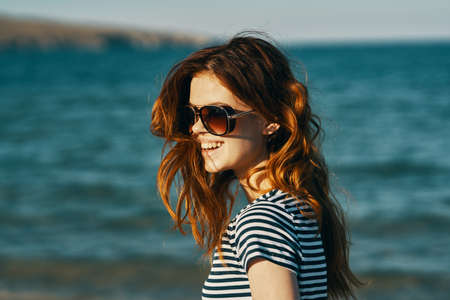 portrait of a red-haired woman in sunglasses in the mountains near the sea and smile laughing travelの写真素材