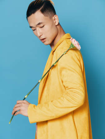 Asian man in a yellow coat with a flower on his shoulder and blue backgroundの写真素材