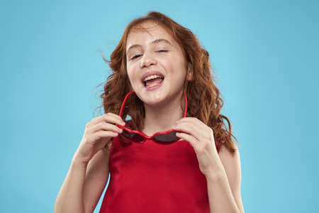 girl with curly hair sunglasses red dress and childhood fun blue backgroundの写真素材