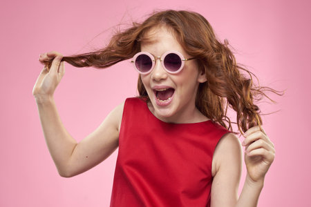 Girl with curly hair dark round glasses fun red dress pink backgroundの写真素材