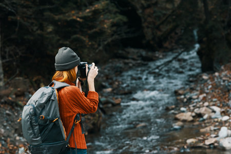 woman with a camera on nature in the mountains near the river and tall trees forest landscape