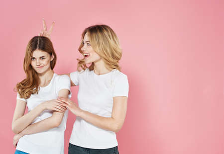 Two pretty women in white t-shirts embrace Friendship pink backgroundの写真素材