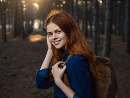 Side view of a woman in a blue shirt in a pine forest with a backpack on her backの写真素材