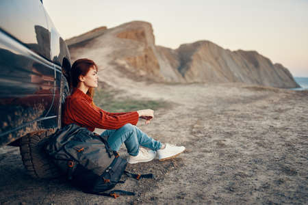 a traveler sits near a car in the mountains in nature and admires the landscape at sunset