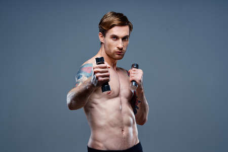 nude man doing sports on gray background and dumbbell tattoo cropped view