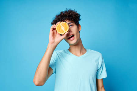 man with curly hair oranges holding fruit studio blue background