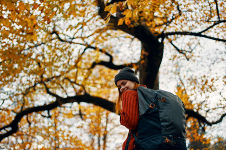 happy travel with a backpack in a red sweater and jeans walks in the park near the treesの写真素材