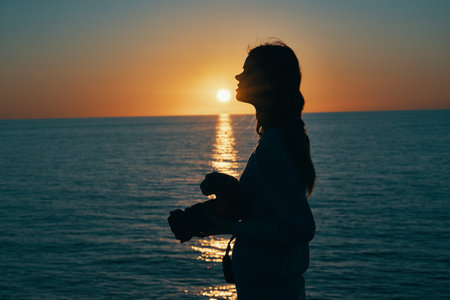 woman photographer with camera at sunset and sea in the backgroundの写真素材