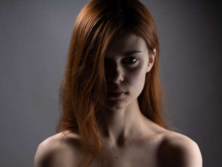 Woman model close-up naked shoulders red hair dark background