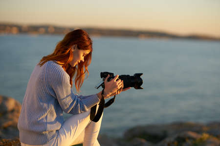 woman with professional camera at sunset by the sea